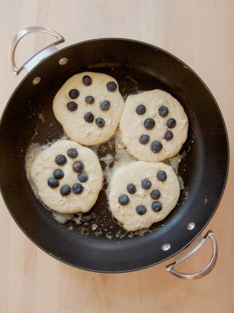 pancakes with blueberries cooking in a skillet